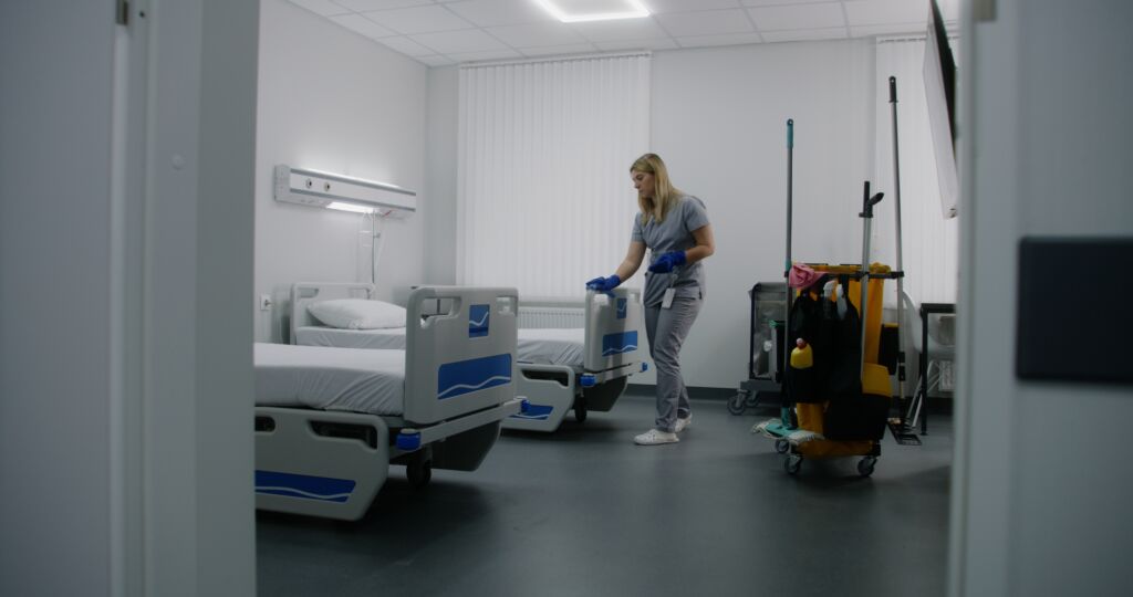 Nurse cleaning bed frames in hospital.