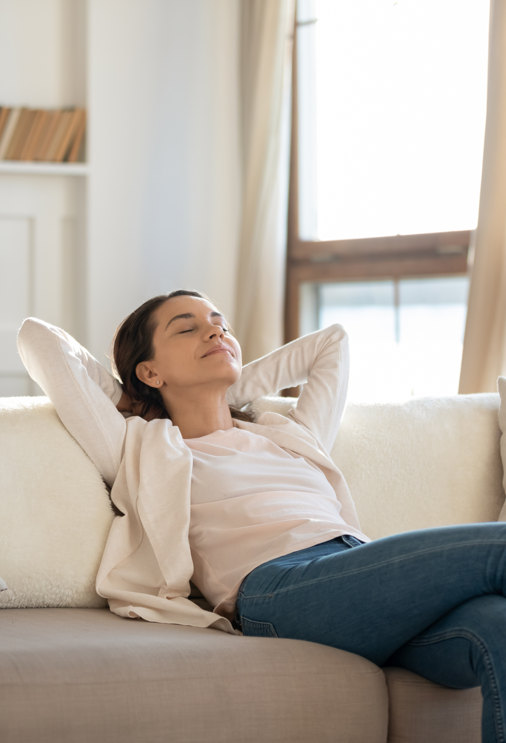 Woman reclining on sofa and inhaling fresh air in a bright, airy room.