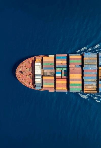 Aerial view of cargo ship carrying containers of various colours across the sea.