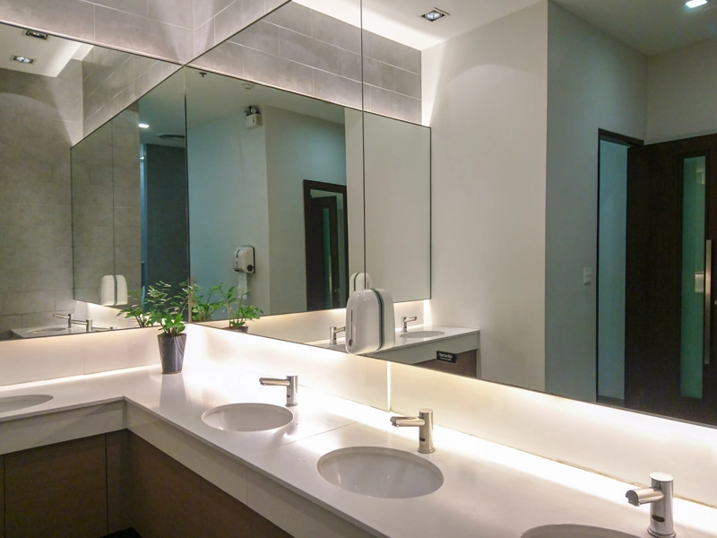 Commercial washroom with mirrored walls, ambient lighting and three white wash basins visible.